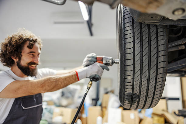 istock Mechanic smiling while changing car tire in garage 2247184243