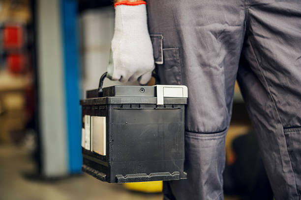 Mechanic holding a car battery, ready to install or replace it in a vehicle. Automotive service and repair concept