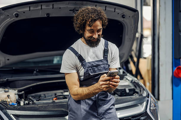 istock Male mechanic smiling using phone at auto repair shop 2247184497