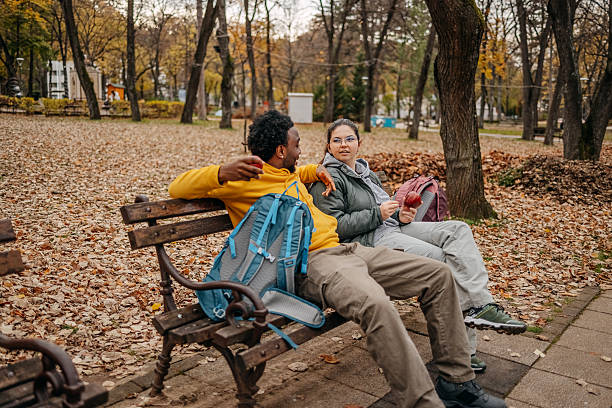 Friends relaxing outdoors sitting on park bench and talking with yellow leaf color around