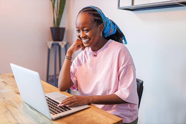 istock Smiling African woman working on laptop in bright workspace with plants 2247187194