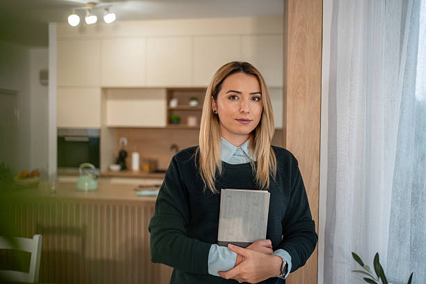 istock Young woman holding book standing in modern kitchen 2247187309