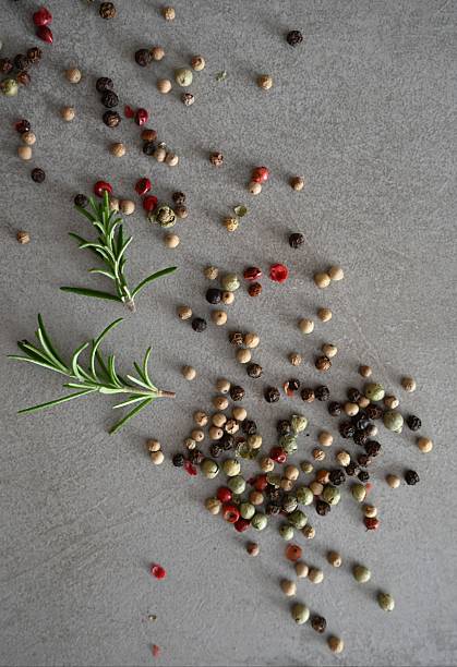 Garlic, rosemary and peppercorns arranged on a white surface with soft daylight shadows. Useful for cookbooks, wellness content and spice branding.