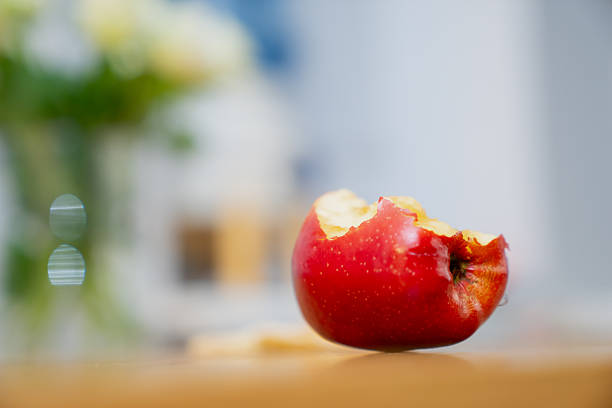 Red apple with bite taken out displayed on bright wooden surface highlighting texture, natural color and everyday snack detail fitting for nutrition, freshness and household food imagery