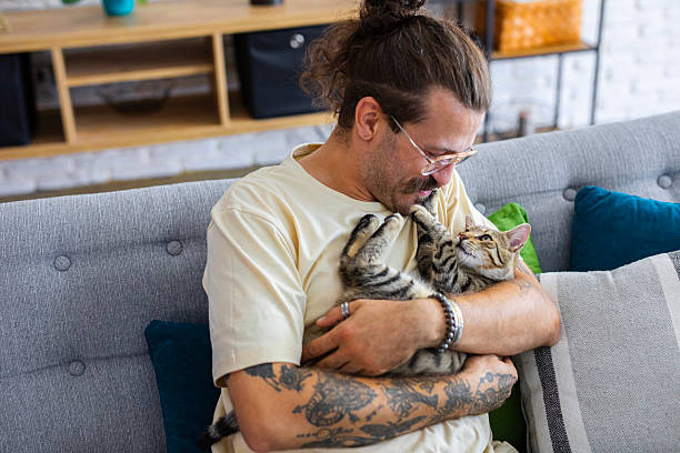 istock Relaxed man sitting on the sofa at home while gently petting his cat 2247190214