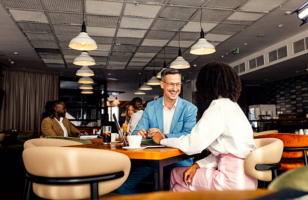 Businessman and female coworker talking about work while using laptop in modern coffee shop.