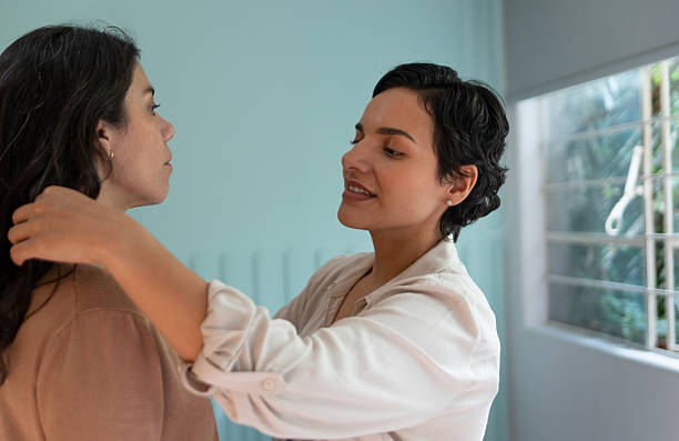 istock lesbian couple being affectionate, one helping the other get ready,  in bedroom 2247195829