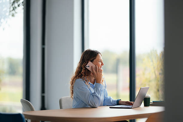 istock Professional Woman In Office On Phone With Laptop And Coffee Cup During Workday 2247197671