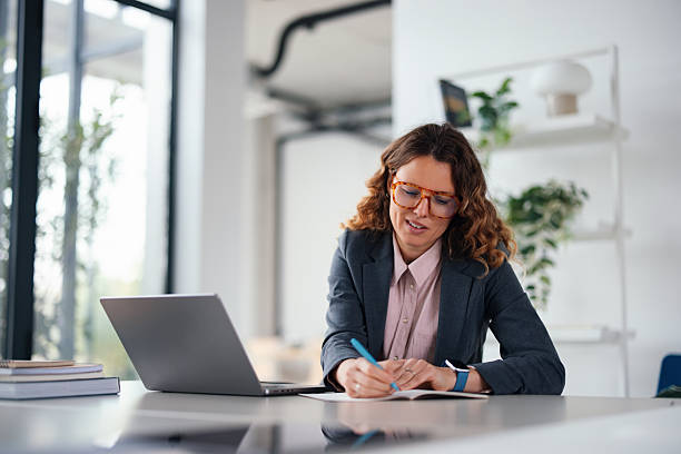 istock Business Woman Working At Desk with Laptop, Writing Notes in Modern Office Setting 2247197879