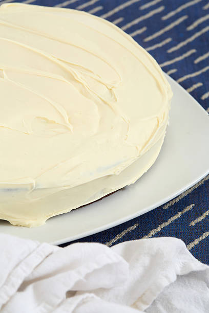 istock Vanilla cake with smooth cream cheese frosting on white plate blue patterned placemat side view 2247222068