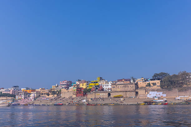 varanasi, uttar pradesh, india- october 27,2025:devotees sit near the ganga as drummers play beside colorful boats on a bright red ghat, capturing city’s spiritual and cultural rhythm