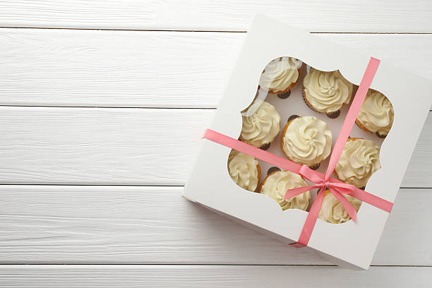 istock Tasty cupcakes with vanilla cream in box on white wooden table, top view. Space for text 2247229085