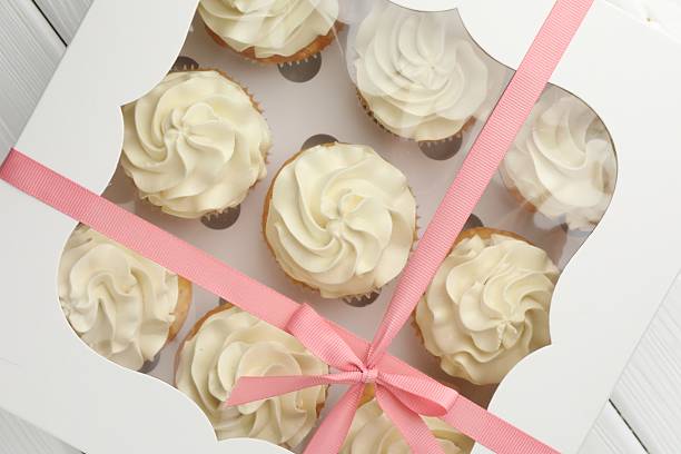 istock Tasty cupcakes with vanilla cream in box on white wooden table, top view 2247229086