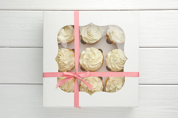 istock Tasty cupcakes with vanilla cream in box on white wooden table, top view 2247229144