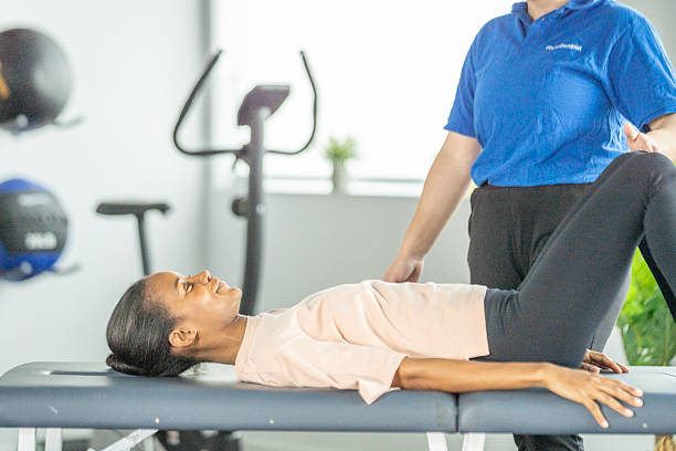 istock Black Woman Performing Leg Raise Exercise on Therapy Table With Trainer in Gym Setting 2247229182