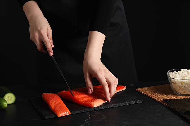 istock Chef cutting salmon for sushi at dark textured table, closeup 2247230606