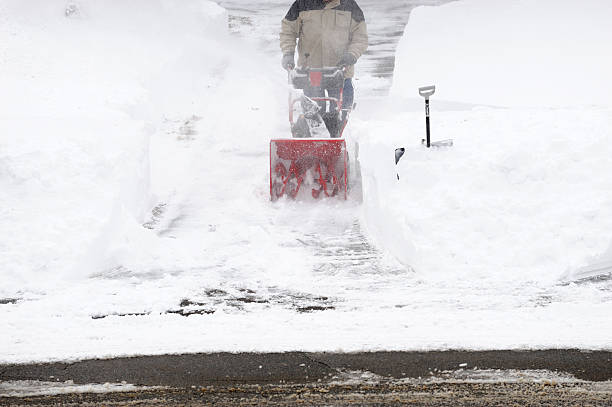 man operating snow blower to remove snow on driveway