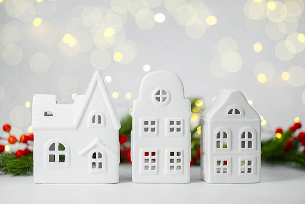 istock Three small white ceramic houses with Christmas decorations and soft bokeh lights in background 2247235299