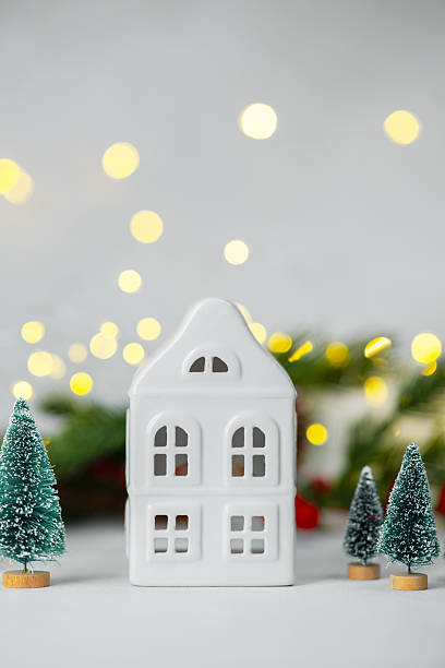 istock White ceramic house with trees and festive lights background, simple holiday decoration concept. 2247235305