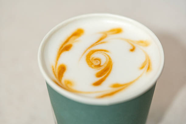 A detailed view of latte art on a creamy coffee drink in a teal cup set on a warm table.
