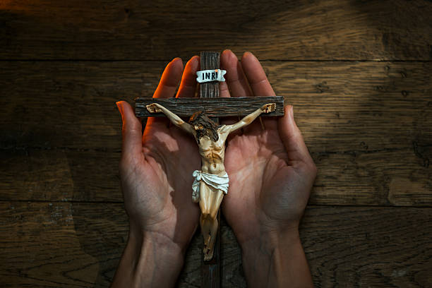 Close-up of human hands gently holding a crucifix of Jesus Christ, symbolizing faith, prayer, and Christian devotion on a wooden surface.