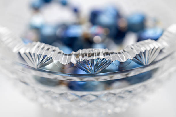 This image shows a macro defocused art style view of vintage blue necklace bead adorning a beautiful scalloped edge antique lead crystal bowl.