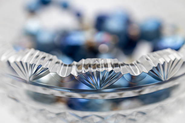 This image shows a macro defocused art style view of vintage blue necklace bead adorning a beautiful scalloped edge antique lead crystal bowl.