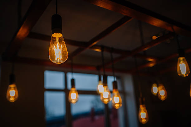 Vintage light bulbs hanging from a wooden ceiling fixture illuminate a cozy interior space, creating a warm ambiance and inviting atmosphere for relaxation and gatherings