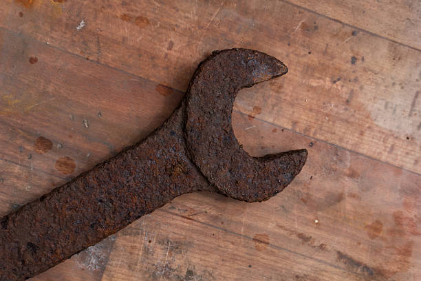 An old, rusty, large wrench lies on a dirty linoleum floor. Background.