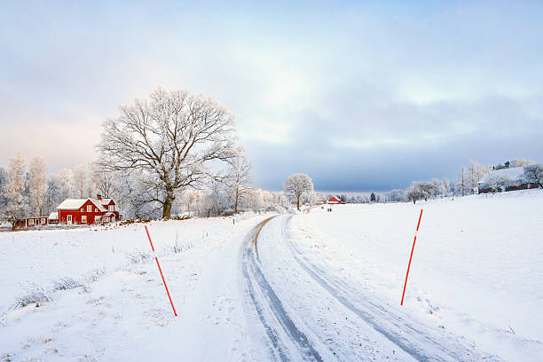 Slippery country road in a rural wintry landscape with a red house