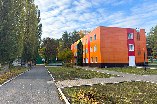 A large orange building with a green roof. The building has a lot of windows. There is a path leading to the building