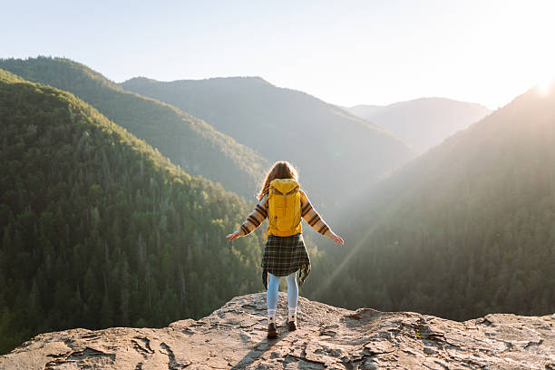 istock Young hiker with yellow hiking backpack standing on cliff at sunset. Real view. 2247245774