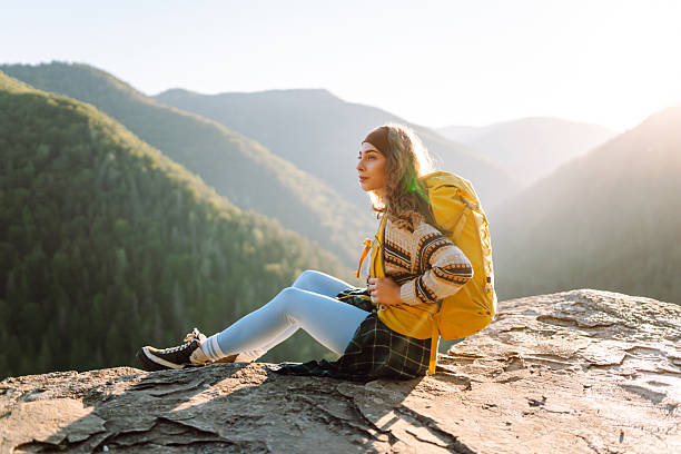istock Young hiker with yellow hiking backpack standing on cliff at sunset. Real view. 2247245814