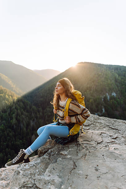 istock Young hiker with yellow hiking backpack standing on cliff at sunset. Real view. 2247245816