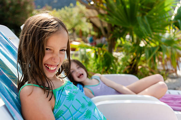 Young sisters smiling and laughing while relaxing on lounge chairs during their summer beach holiday