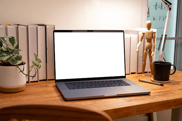 istock Modern laptop with a blank white screen mockup placed on a wooden desk in a stylish, cluttered workspace with books and decor. 2247252949