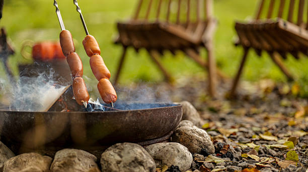 Sausages grilling over a campfire on skewers, outdoor cooking scene