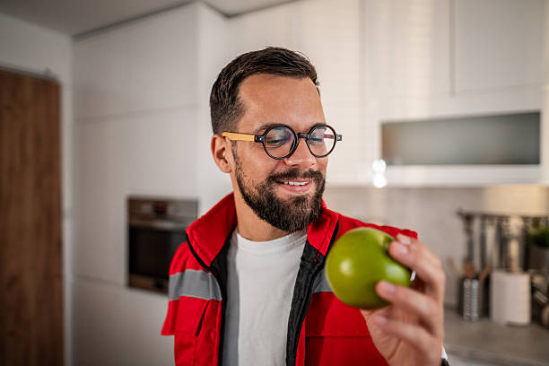 Smiling paramedic man in uniform taking a healthy fruit snack break in the kitchen, prioritizing well-being and a balanced diet during his busy workday