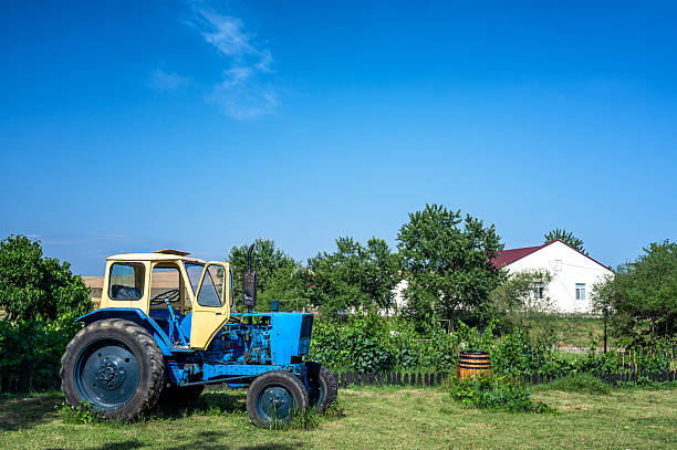 A tractor stands next to a rural house surrounded by plants and greenery in Hacihetemli, Azerbaijan.