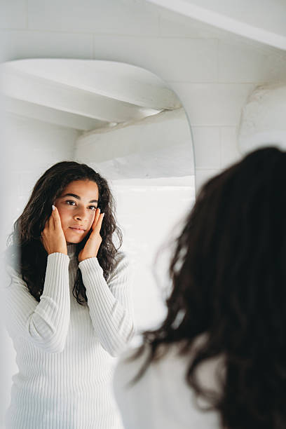 istock Young woman checking skin while looking in mirror 2247258750