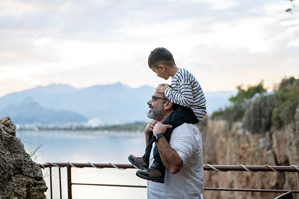 Family, children and boy sitting on the shoulders of his father outdoor while bonding from below. Fun, kids and love with a man carrying his son outside while spending time together being playful