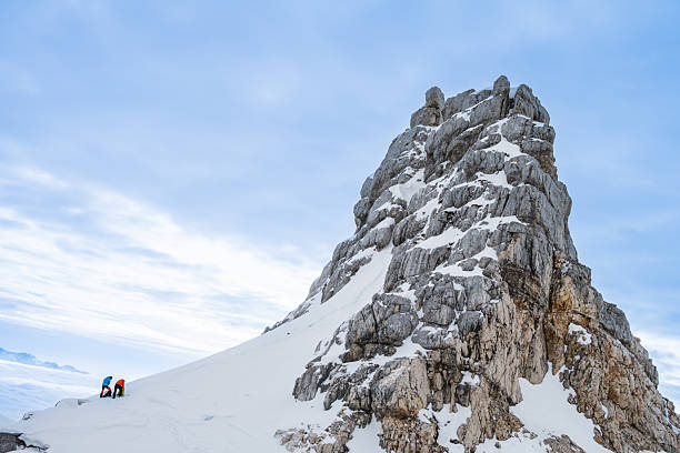 Two individuals pause on a snowy slope, enjoying the serene view of a misty mountain range. The winter landscape offers a tranquil backdrop as they take a moment amidst their mountaineering journey.