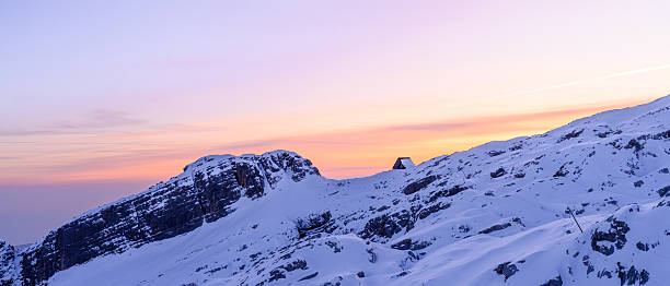 Snow-draped alpine peaks basking in the soft glow of twilight, with the sky transitioning from day to night, casting gentle hues over the landscape.