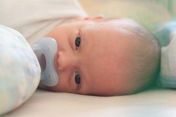 istock Infant lies on back in cot with a pacifier looking directly at camera with big blue eyes 2247267341
