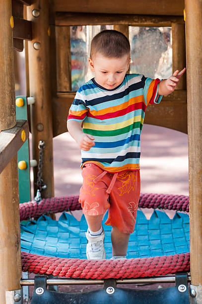 istock Young boy plays on rope bridge in playground structure during the daytime in the Summer 2247267425