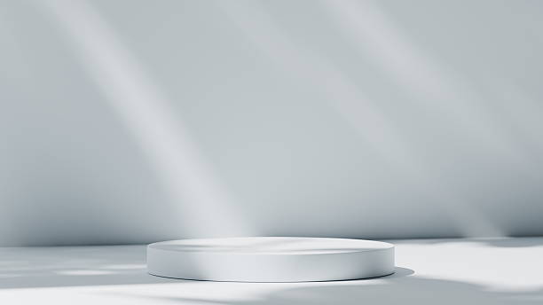 istock round white platform sits in a bright, minimalist room. Soft shadows from sunlight create a calming atmosphere against the plain walls and floor. 3d render 2247272146