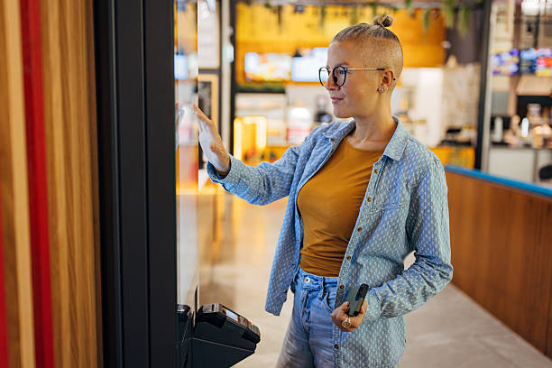 istock Woman placing an order using a digital touchscreen kiosk at a modern quick-service restaurant. Female customer interacting with self-order technology 2247272546