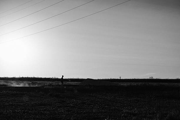 A lone figure is running across an open field, seen in striking silhouette against a bright sky at sunset