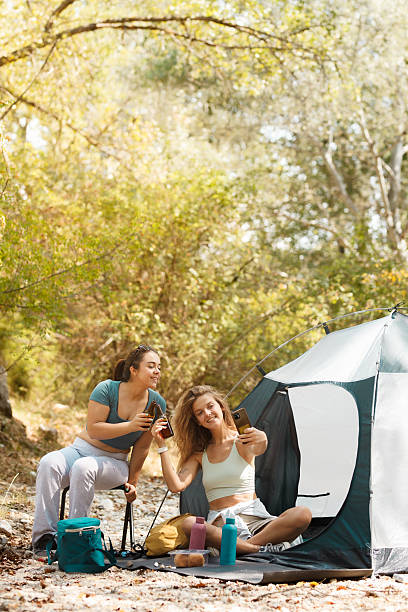 istock Two friends enjoy a relaxing day at a campsite, taking selfies and sharing drinks in a peaceful forest setting during autumn 2247277069