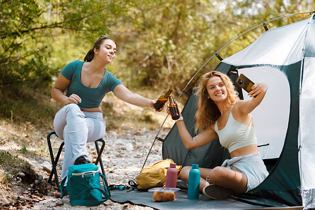 istock Friends enjoying beverages and taking selfies while camping in a lush forest during a sunny day 2247277071